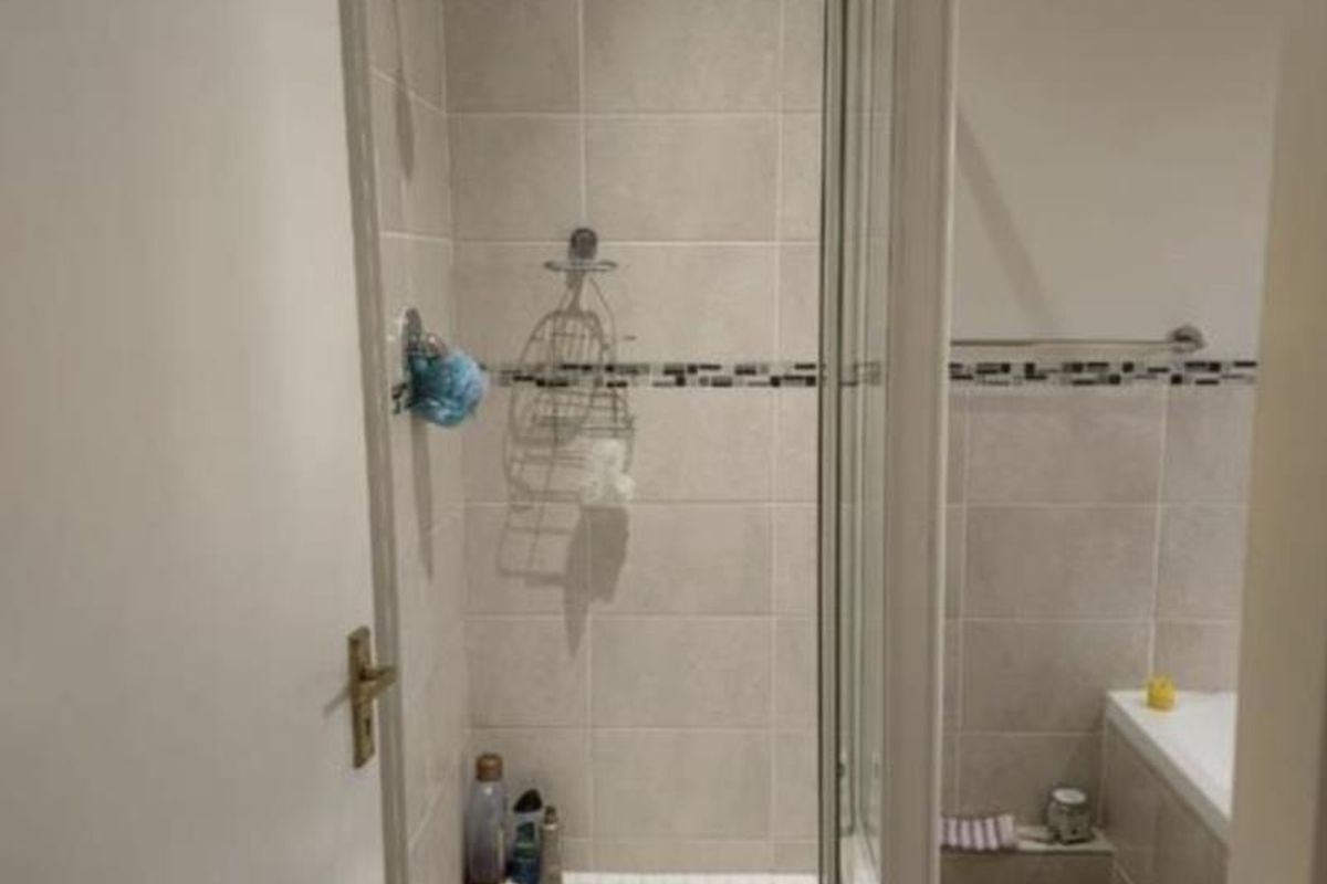 A functional bathroom featuring a tiled shower enclosure with a glass door and a separate bathtub with neutral wall tiling.