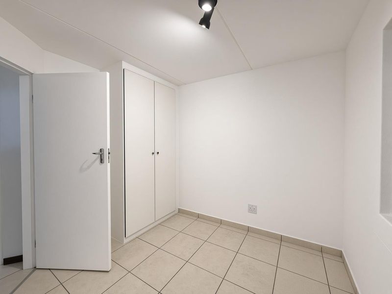 A clean, empty bedroom featuring neutral tiled flooring, a built-in wardrobe, and a modern spotlight fixture, ready for personalization.