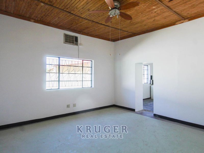 An empty living room featuring a timber ceiling, ceiling fan, and wall-mounted air conditioning unit, with direct access to an adjacent room.