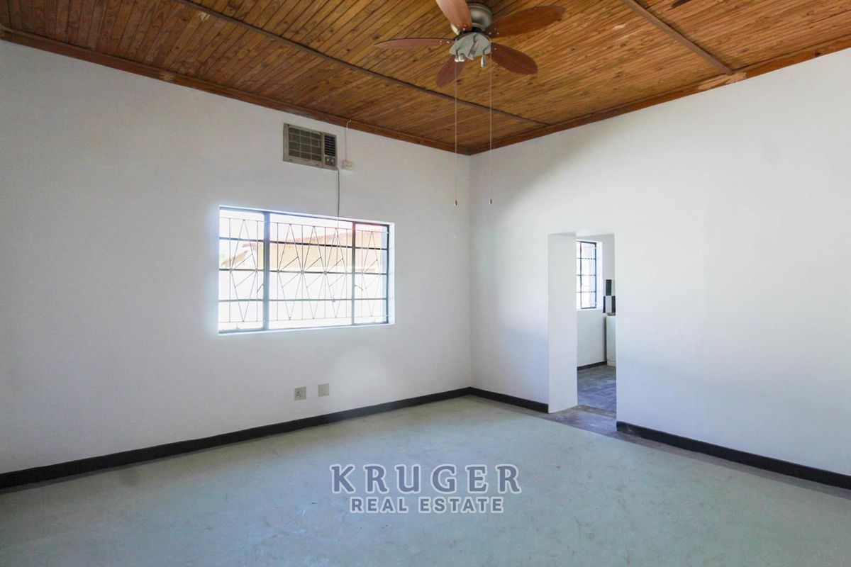 An empty living room featuring a timber ceiling, ceiling fan, and wall-mounted air conditioning unit, with direct access to an adjacent room.
