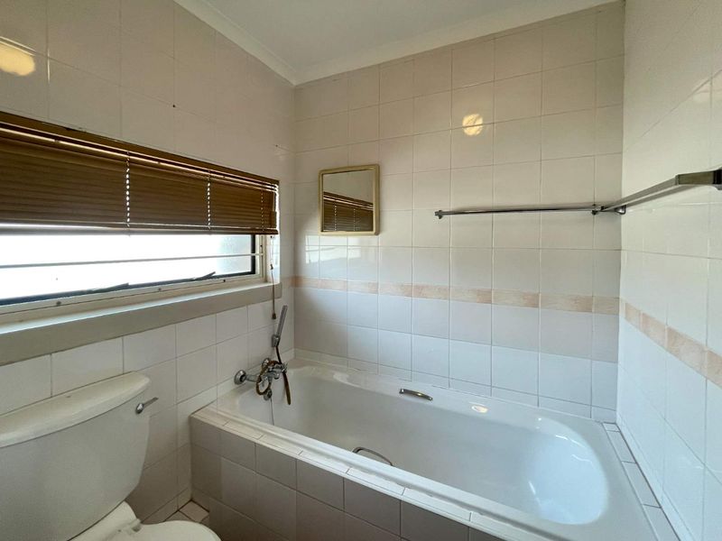 A dated bathroom featuring a built-in bathtub, tiled walls, and a standard toilet, offering a functional space ready for modernization.