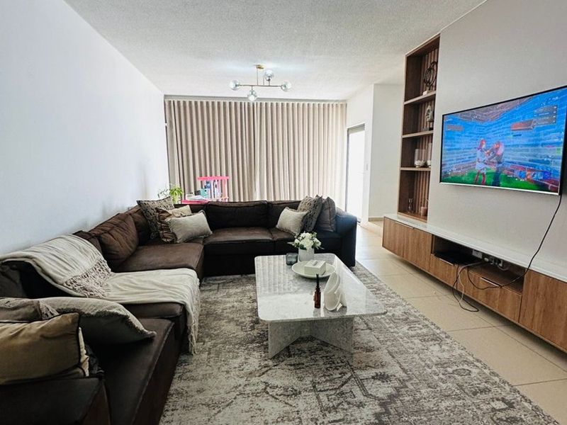 Spacious living room featuring tiled flooring, a custom built-in media unit with shelving, and modern lighting, leading to a bright patio area.