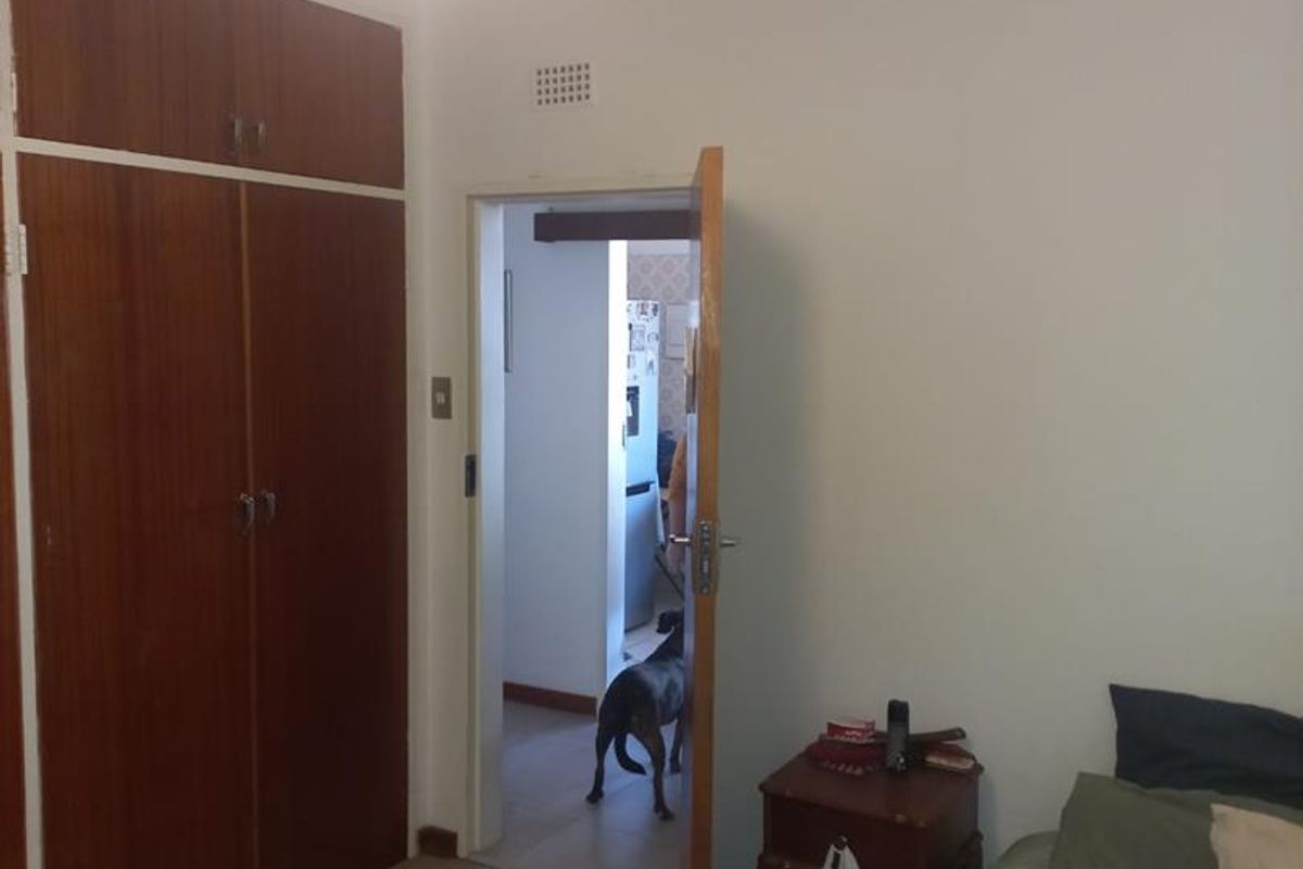 A bedroom featuring built-in wooden cupboards and carpeted flooring, with a doorway leading to an adjacent room.