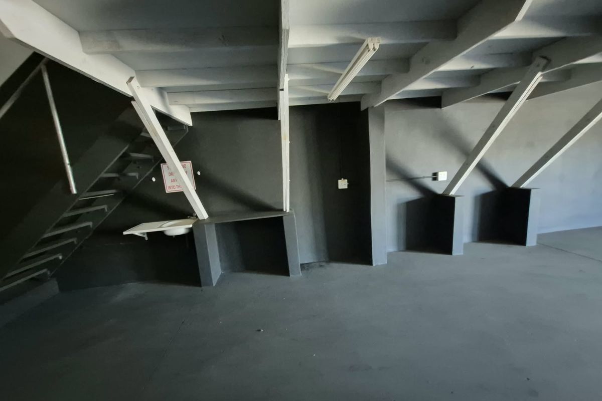 An open-plan industrial utility space featuring exposed timber ceiling beams, a concrete floor, a built-in utility sink, and a staircase.