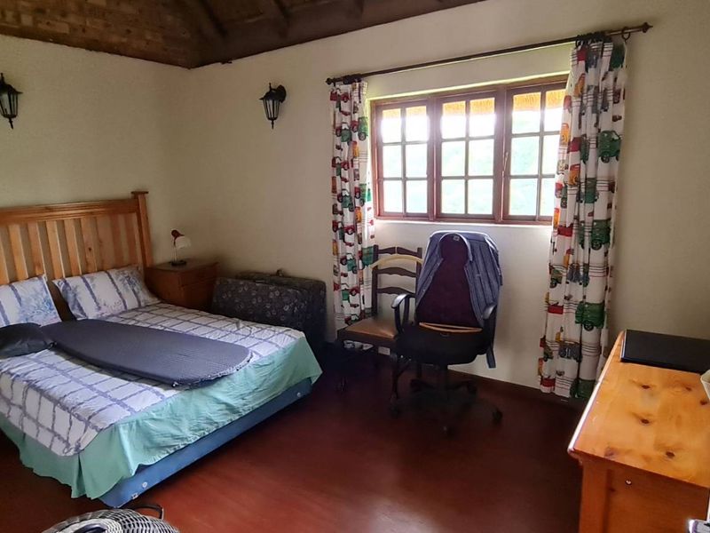 A bedroom featuring exposed timber ceiling beams, laminate flooring, and natural light through timber-framed windows.