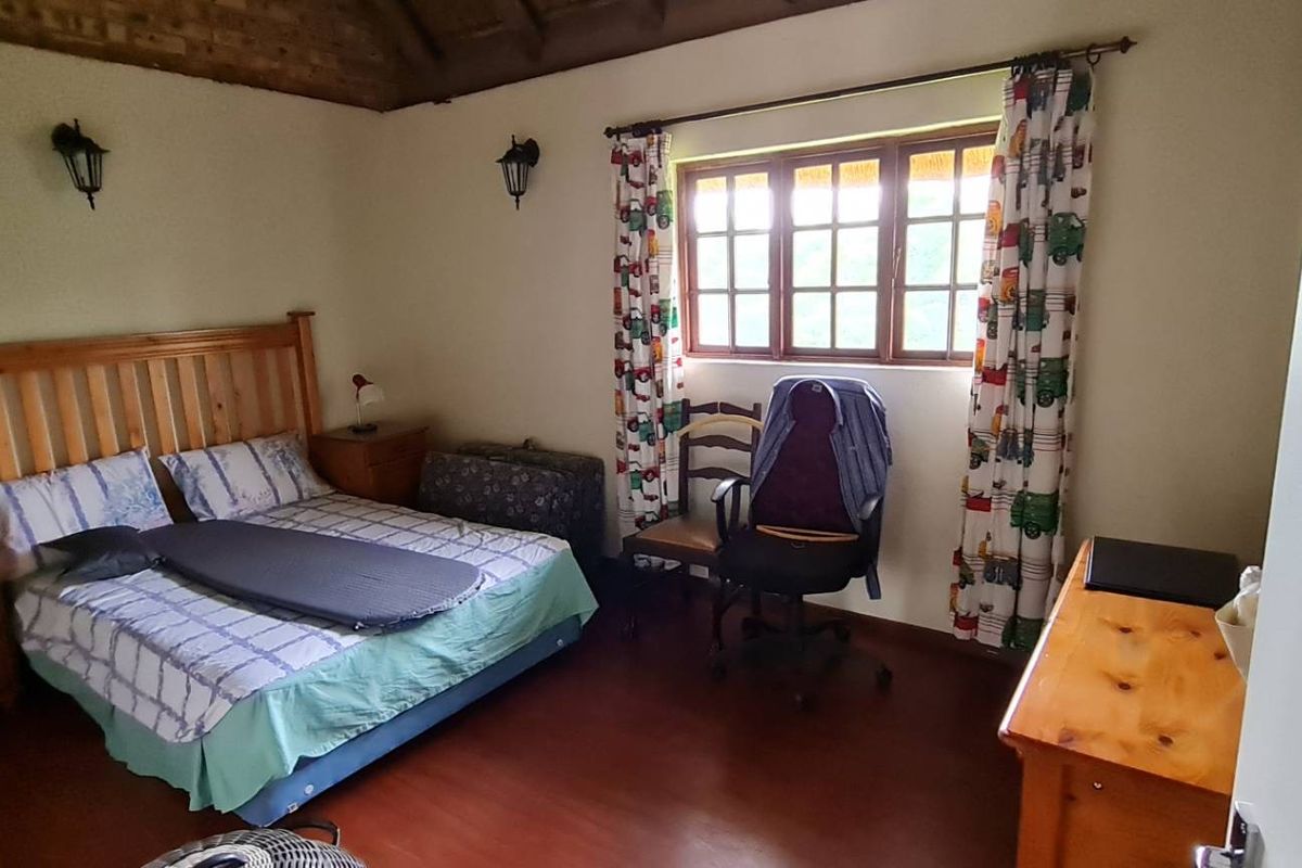 A bedroom featuring exposed timber ceiling beams, laminate flooring, and natural light through timber-framed windows.