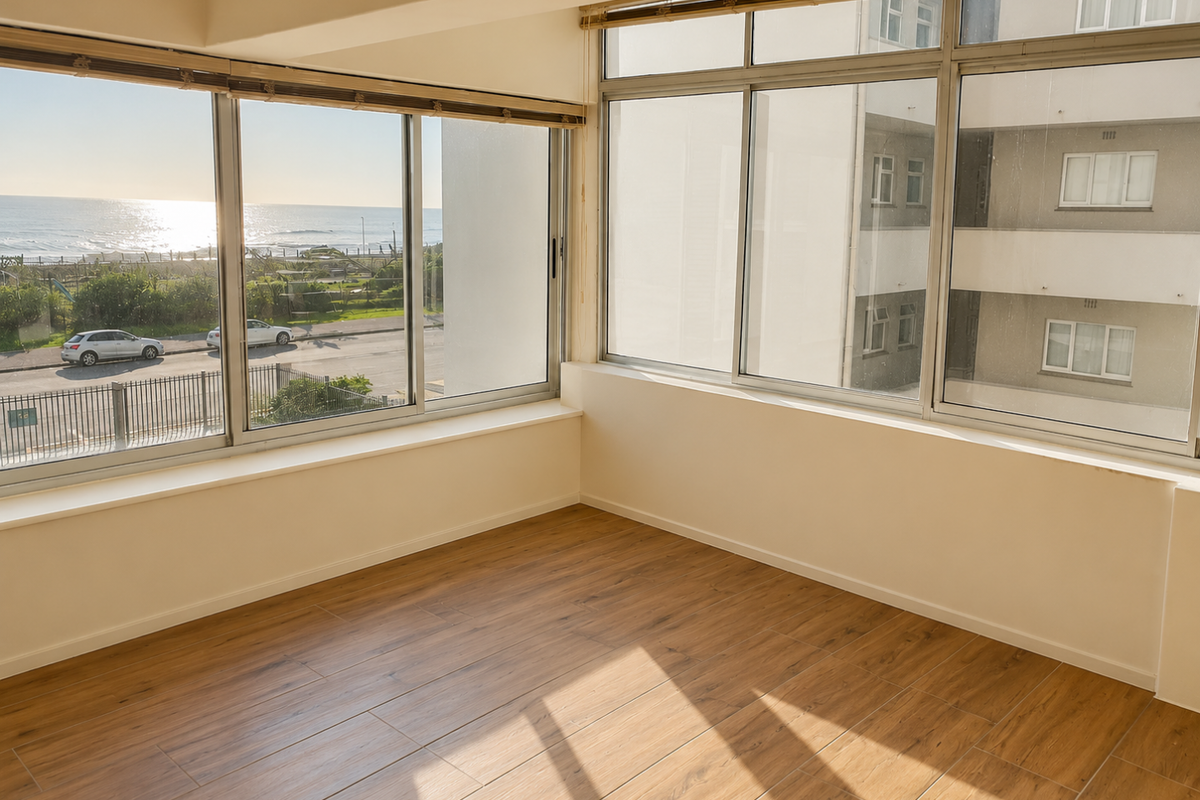 A bright, empty living area featuring modern wood-look laminate flooring and expansive windows offering natural light and coastal views.