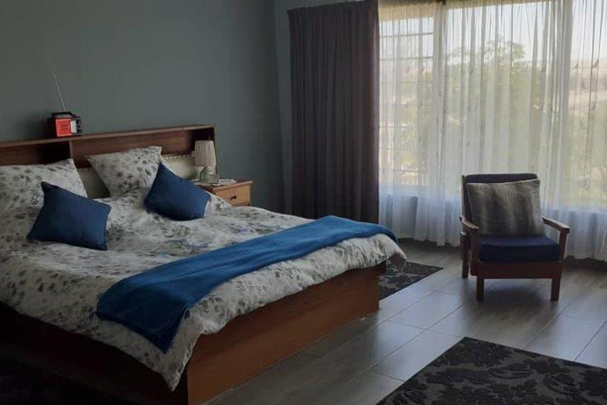 A spacious bedroom featuring large windows with natural light, tiled flooring, and a built-in headboard unit.