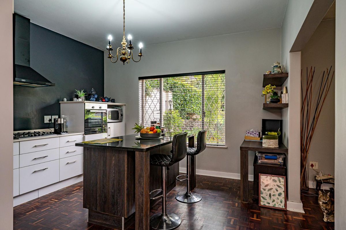 Modern kitchen featuring a central island, built-in oven, gas hob, extractor fan, and dark wood cabinetry, complemented by parquet flooring and natural light.