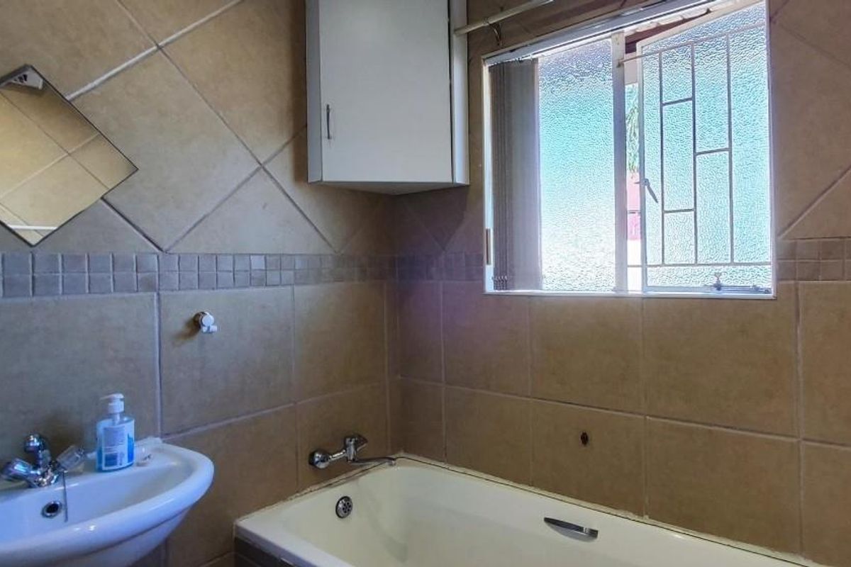 A functional bathroom featuring a bathtub, wall-mounted basin, and tiled walls with a window providing natural light.