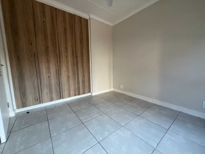 A clean, empty bedroom featuring modern wood-finish built-in cupboards and neutral grey floor tiles, providing a versatile space ready for personalization.