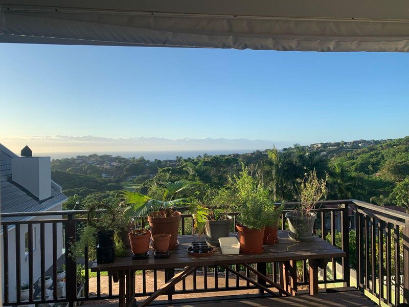 A spacious balcony featuring a retractable awning and metal railing, offering expansive scenic views of the surrounding landscape and distant coastline.