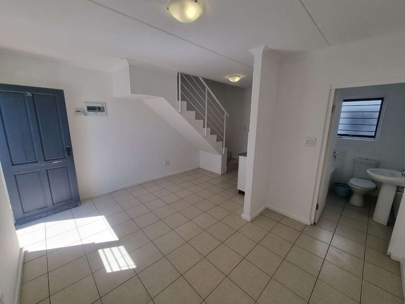 An open-plan living area featuring tiled flooring, a staircase with metal railing, and an adjacent guest bathroom with a pedestal basin and toilet.