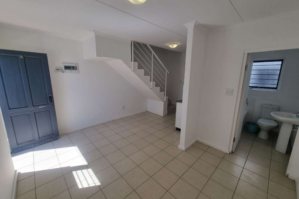 An open-plan living area featuring tiled flooring, a staircase with metal railing, and an adjacent guest bathroom with a pedestal basin and toilet.