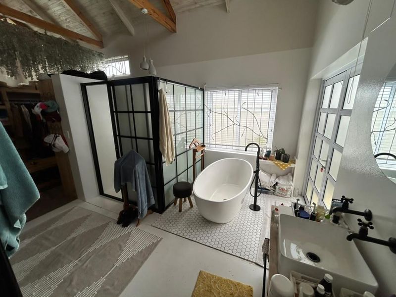 Modern bathroom featuring a freestanding bathtub, black-framed glass shower, vessel sink, and vaulted ceilings with exposed timber beams.