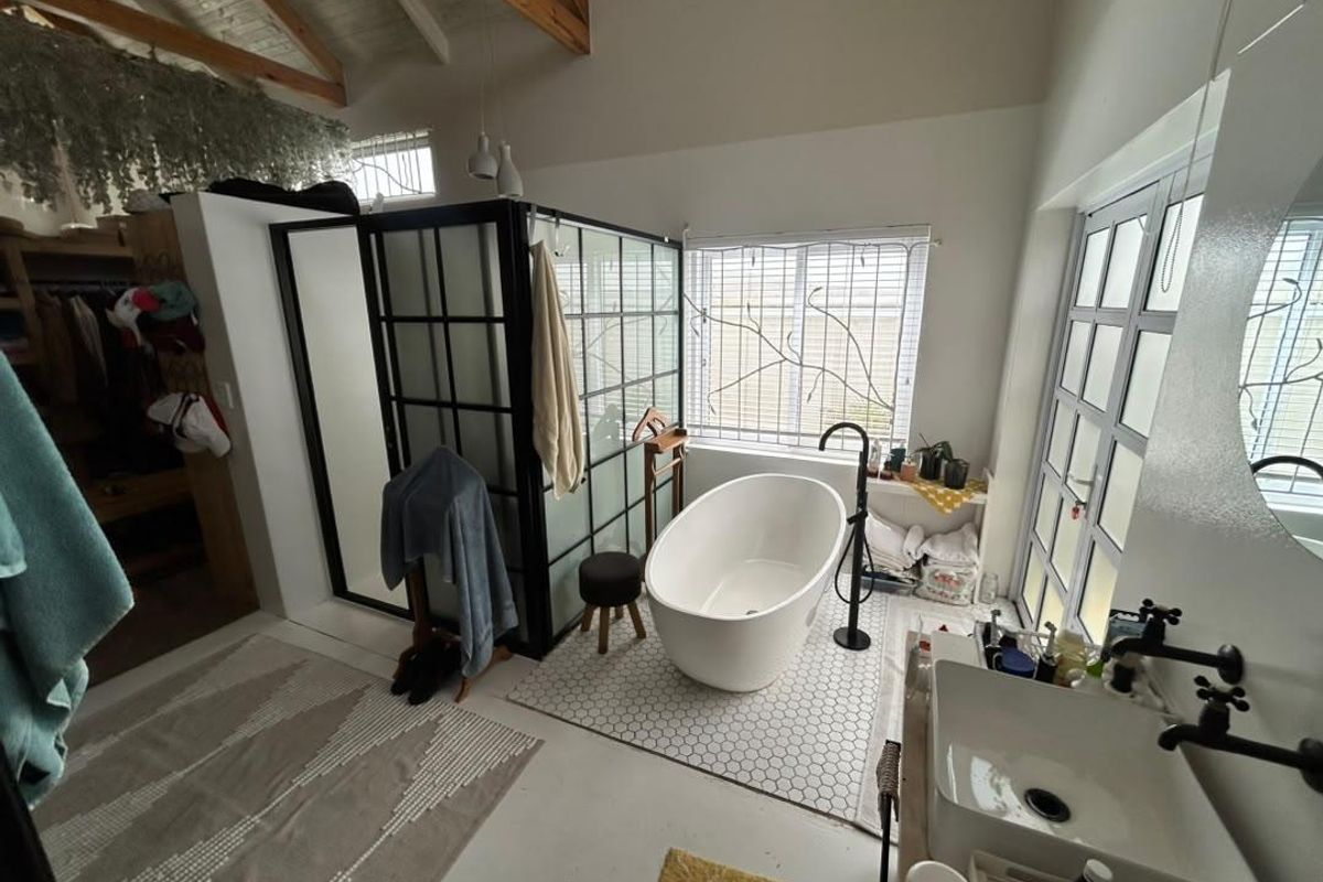 Modern bathroom featuring a freestanding bathtub, black-framed glass shower, vessel sink, and vaulted ceilings with exposed timber beams.
