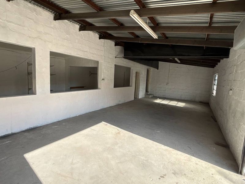 An open-plan industrial utility space featuring exposed timber rafters, corrugated metal roofing, concrete flooring, and large wall openings, suitable for storage or workshop use.