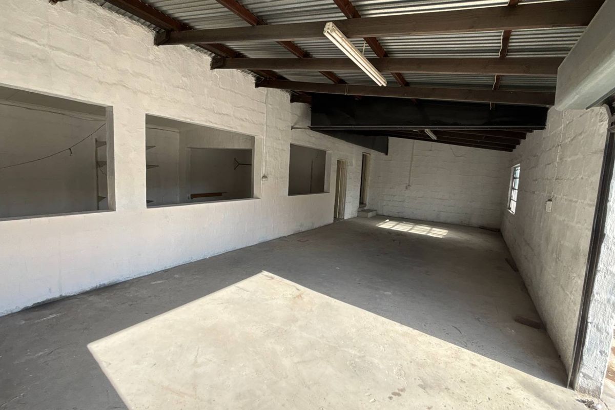 An open-plan industrial utility space featuring exposed timber rafters, corrugated metal roofing, concrete flooring, and large wall openings, suitable for storage or workshop use.