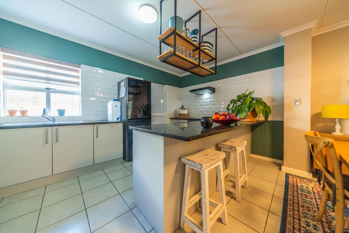 A functional kitchen featuring a breakfast bar, subway tile backsplash, granite countertops, and a suspended industrial-style shelving unit.