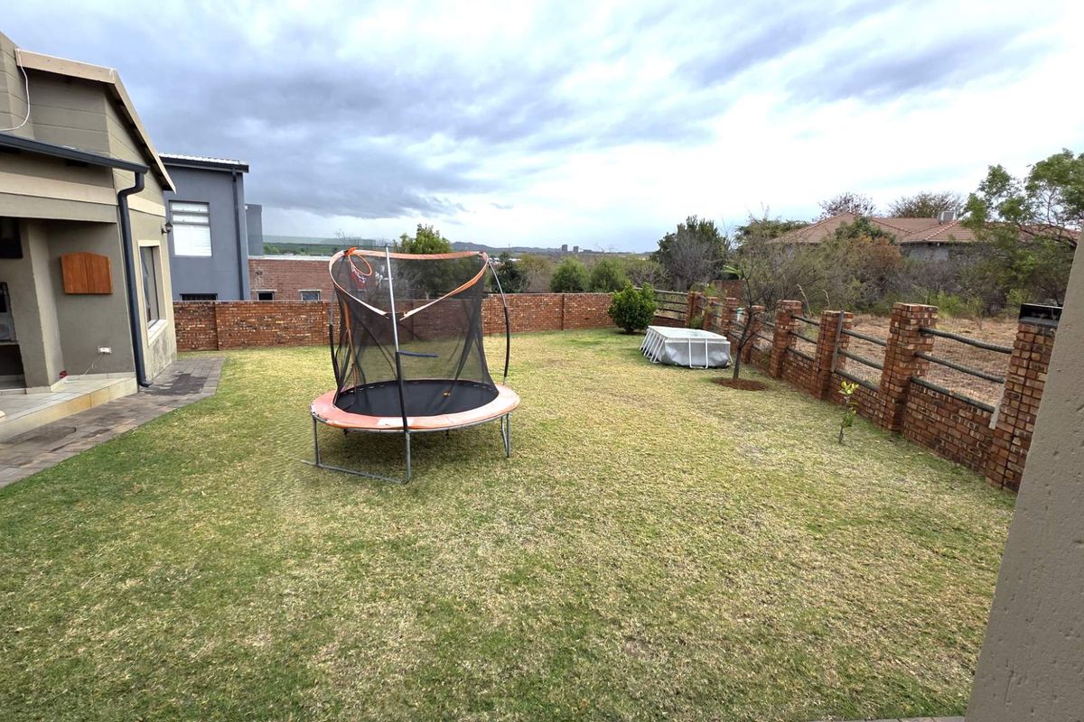 A spacious rear garden featuring a lawn, brick boundary walls, and a covered patio area attached to the main house structure.