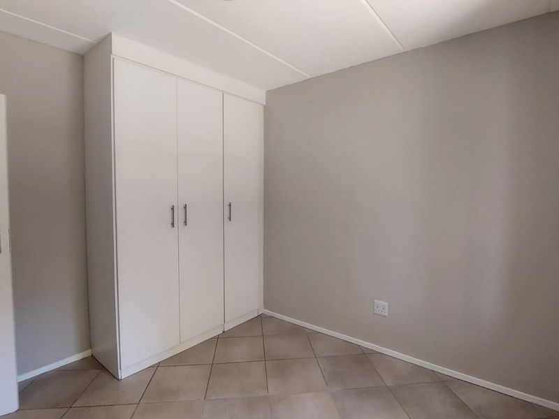 A clean, empty bedroom featuring neutral wall paint, tiled flooring, and a white built-in wardrobe with modern handles.