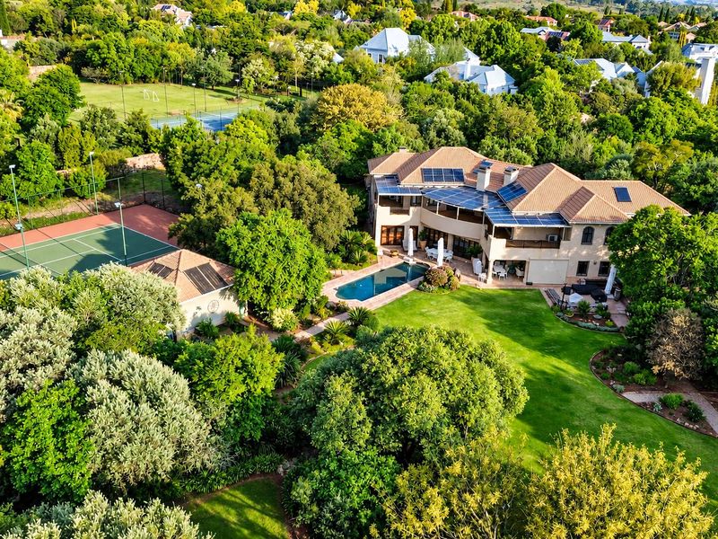 Aerial view of a large residential property featuring a swimming pool, private tennis court, solar panels, and extensive landscaped gardens.