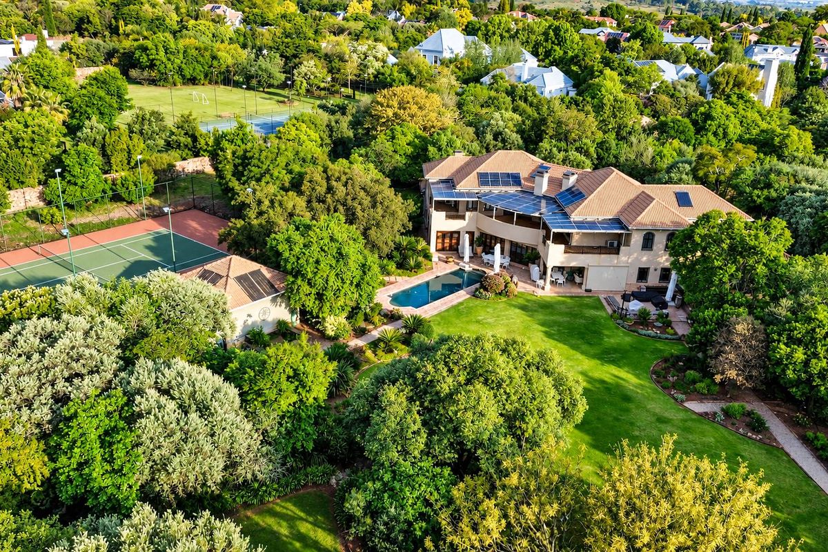 Aerial view of a large residential property featuring a swimming pool, private tennis court, solar panels, and extensive landscaped gardens.