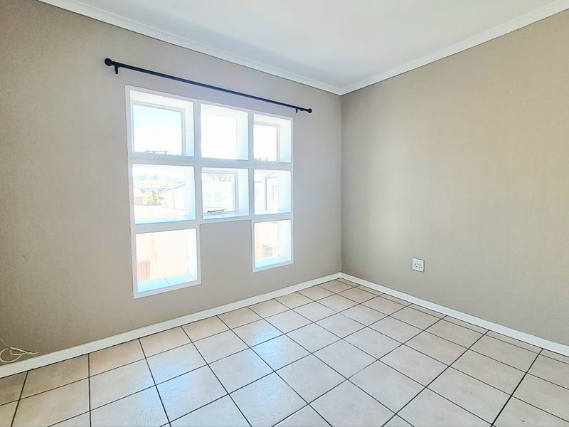 A bright, empty bedroom featuring neutral wall paint, tiled flooring, and a distinctive grid-pattern window with an installed curtain rod.