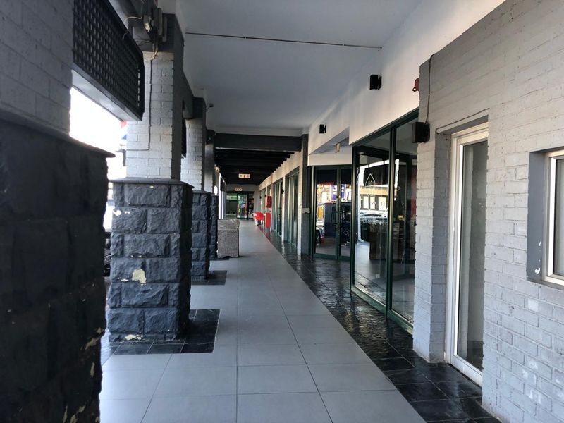 A covered retail walkway featuring tiled flooring, brick columns, and glass storefronts, providing a clean and accessible entrance area for commercial units.