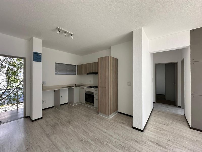 Open-plan kitchen and living area featuring modern laminate flooring, built-in cabinetry, and integrated appliances, with direct access to a balcony.
