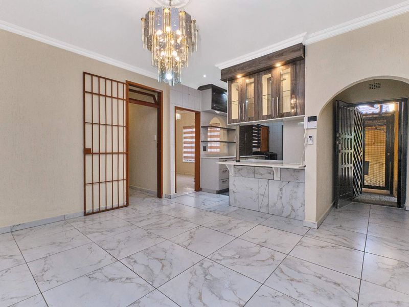 Open plan living area featuring marble-look floor tiles, a built-in breakfast bar with overhead cabinetry, and an elegant chandelier, leading to a secure entrance.