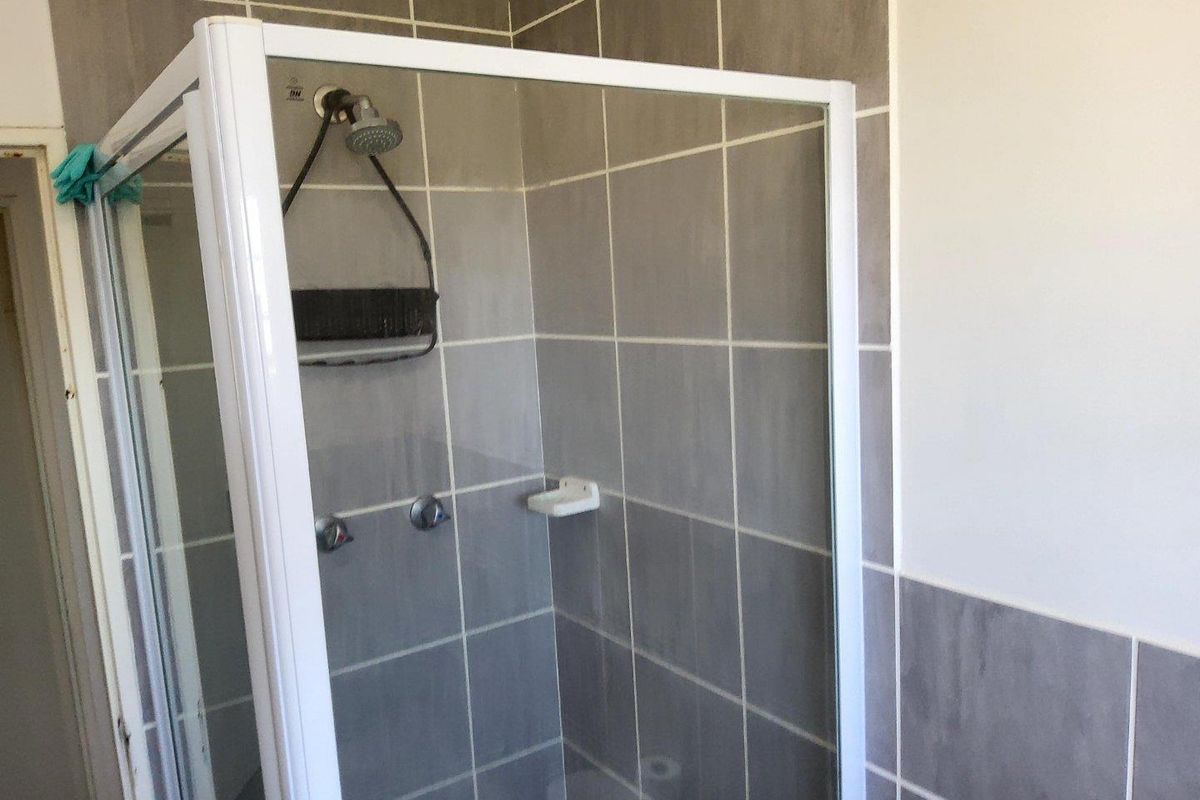 A functional bathroom shower enclosure featuring grey wall tiles, a white frame, and standard chrome shower fixtures.