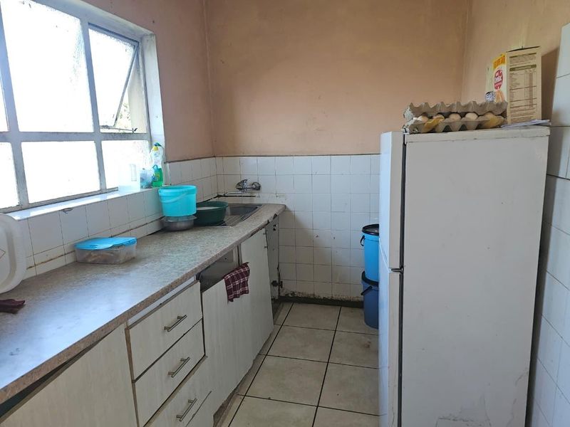 A compact kitchen featuring laminate countertops, a stainless steel sink, tiled backsplash, and built-in cabinetry, requiring cosmetic updates to improve its overall condition.