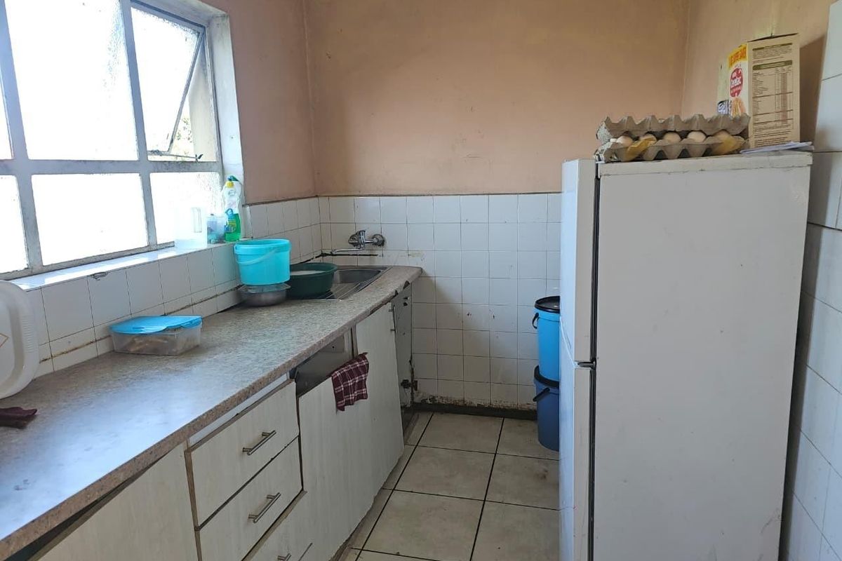 A compact kitchen featuring laminate countertops, a stainless steel sink, tiled backsplash, and built-in cabinetry, requiring cosmetic updates to improve its overall condition.