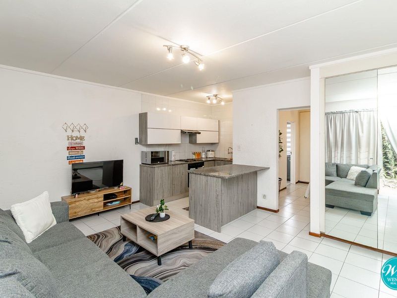 Open-plan living area featuring a modern kitchen with granite countertops, tiled flooring, and mirrored built-in storage, creating a bright and functional space.