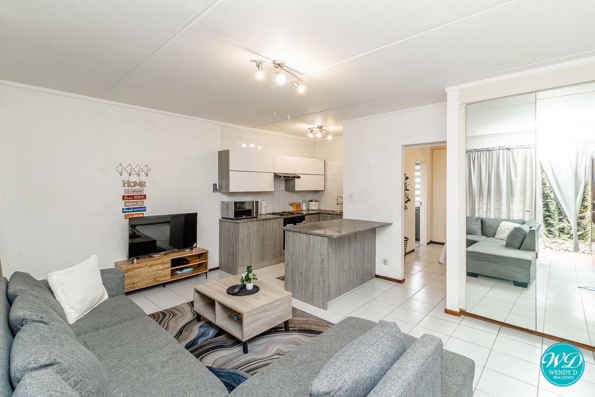 Open-plan living area featuring a modern kitchen with granite countertops, tiled flooring, and mirrored built-in storage, creating a bright and functional space.