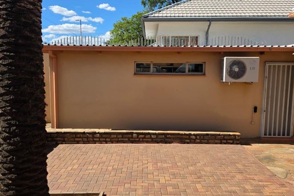 A paved outdoor courtyard area featuring a low stone retaining wall, security spikes on the perimeter wall, and an external air conditioning unit.