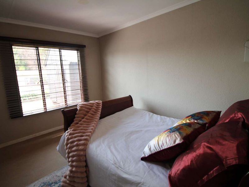 A standard bedroom featuring carpeted flooring, neutral wall finishes, and fitted venetian blinds on the window.