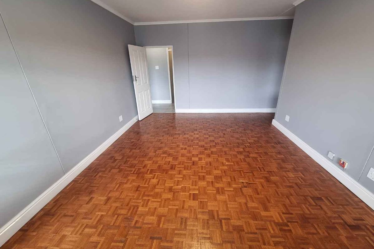 A spacious, empty living area featuring well-maintained parquet flooring, neutral grey walls, and classic coving detail.
