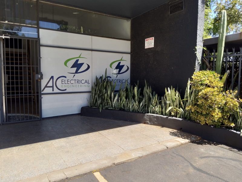 Front entrance of a commercial retail property featuring a paved driveway, security gate, and glass storefront with signage.