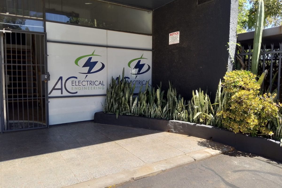 Front entrance of a commercial retail property featuring a paved driveway, security gate, and glass storefront with signage.