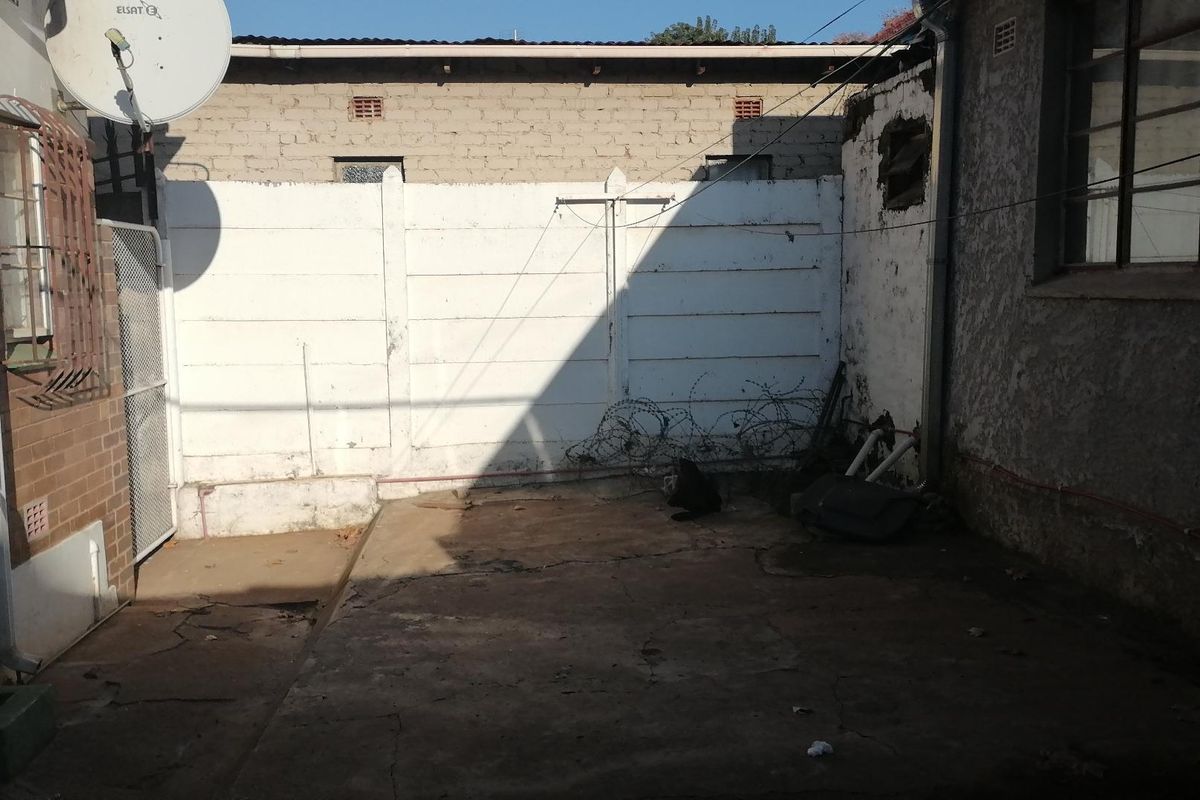 A rear exterior courtyard area featuring a concrete patio, perimeter boundary wall, and exposed building exterior finishes.