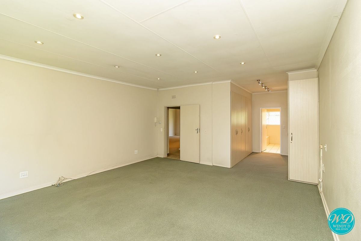 Spacious bedroom featuring neutral walls, carpeted flooring, recessed downlighting, and extensive built-in cupboard storage with an adjoining en-suite bathroom.