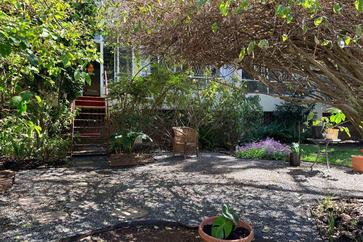 A rear garden area featuring a gravel surface, stepping stones, and a metal staircase providing access to the elevated apartment level.