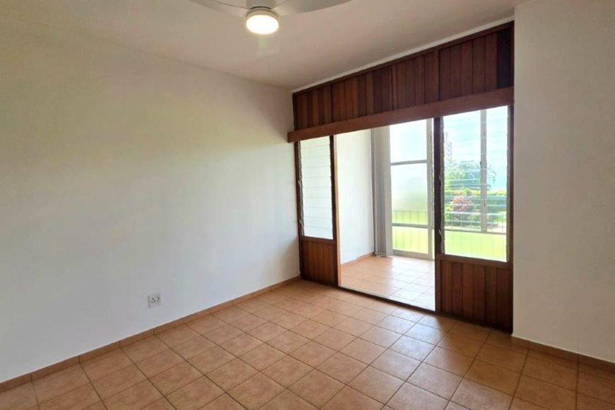 A bright, empty bedroom featuring tiled flooring, a ceiling fan, and large wooden-framed sliding doors providing access to an outdoor balcony area.