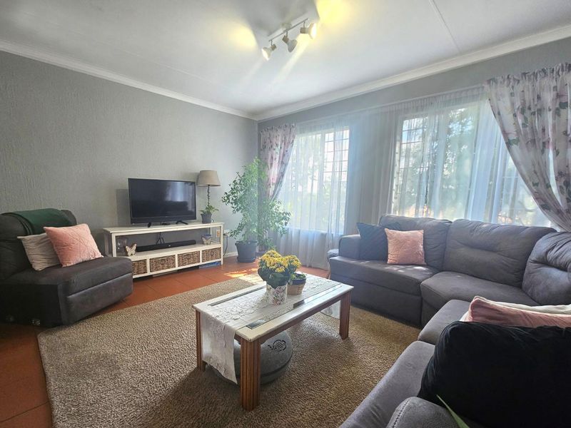 A comfortable living room featuring tiled flooring, coving, and track lighting, with large windows allowing for natural light.