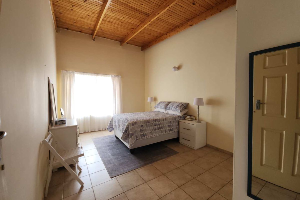 Spacious bedroom featuring high vaulted timber ceilings, tiled flooring, and large window providing ample natural light.