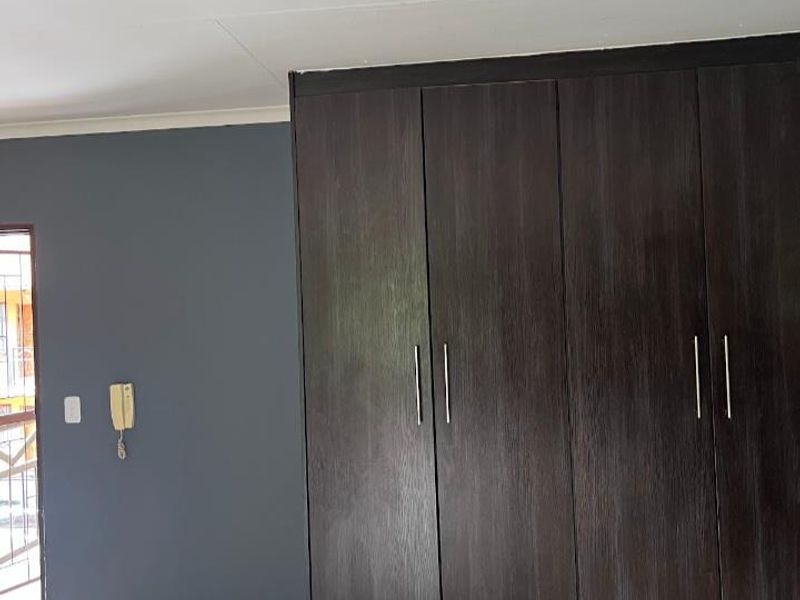 A clean, empty bedroom featuring dark wood built-in cupboards, tiled flooring, and a feature wall with an integrated intercom system.