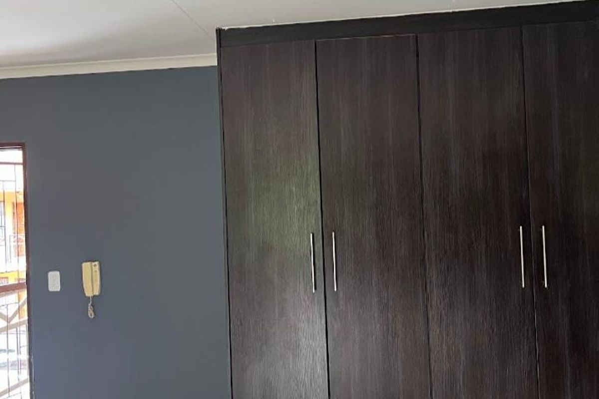 A clean, empty bedroom featuring dark wood built-in cupboards, tiled flooring, and a feature wall with an integrated intercom system.