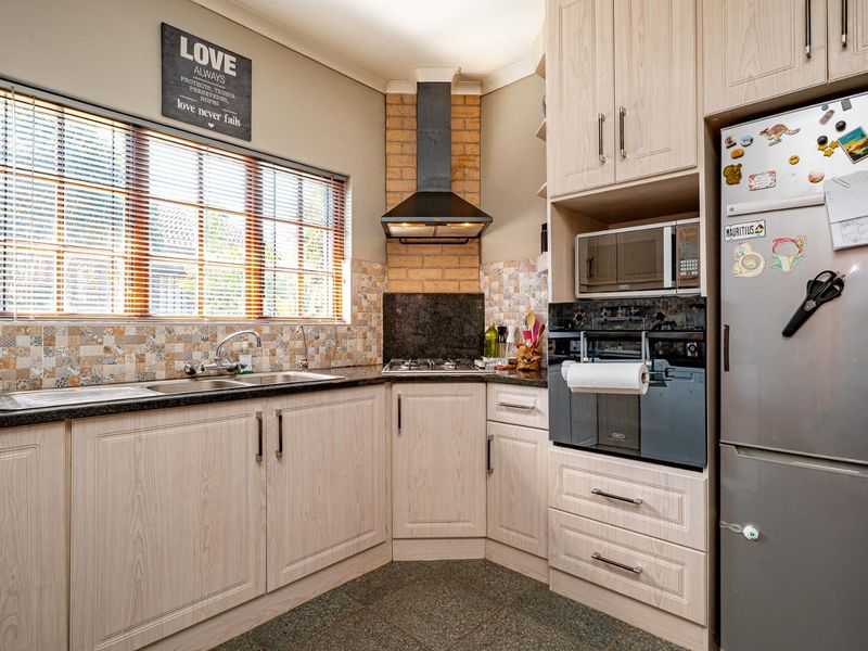 Functional kitchen featuring light wood-grain cabinetry, granite countertops, built-in oven, gas hob with extractor, and a brick feature wall.
